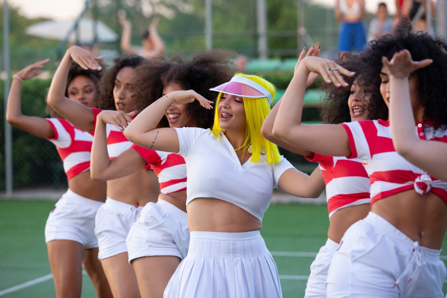 La donna con il caschetto giallo al centro di un gruppo di ballerine in polo a righe, tutte con le braccia in coreografia