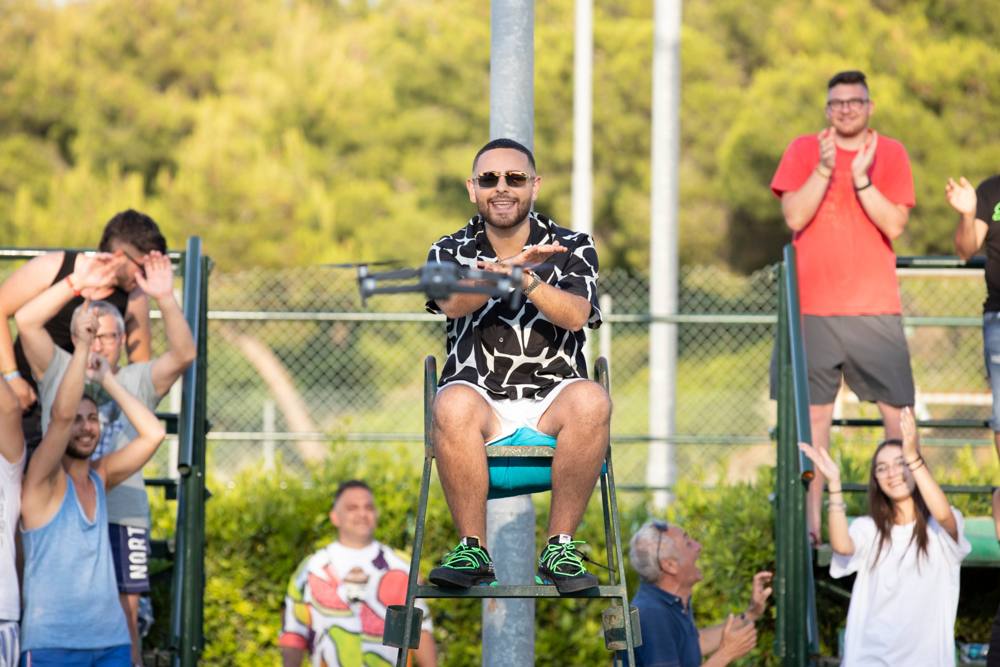 L'uomo sul seggiolone incrocia le braccia davanti a un drone in volo, tra il pubblico che applaude