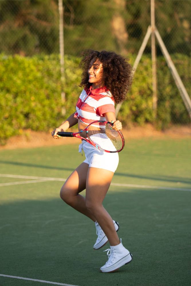 Una ballerina con la racchetta da tennis rossa salta sul campo con un grande sorriso, nella luce dorata