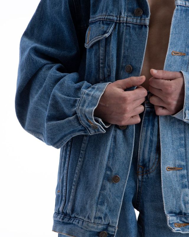 Dettaglio di una giacca di jeans: due mani chiudono i bottoni sul davanti