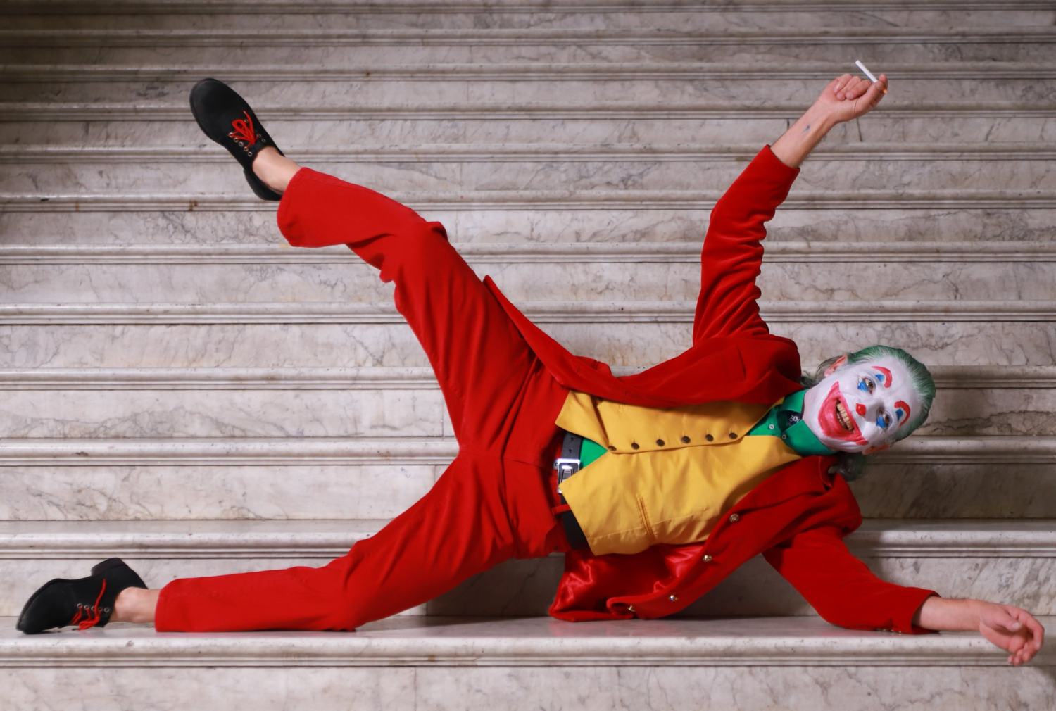 Joker disteso di lato sui gradini con una gamba alzata e la sigaretta in mano