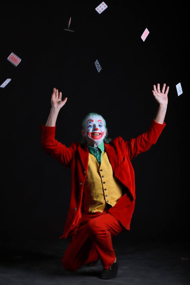Joker in ginocchio con le braccia al cielo mentre lancia le carte da gioco