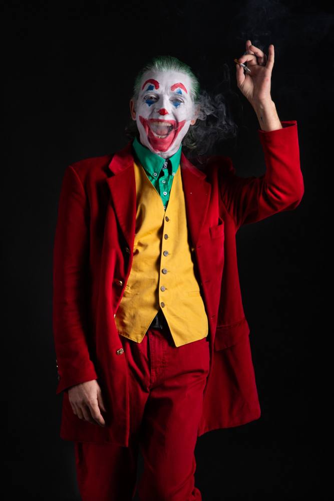 Joker che ride a bocca aperta su fondo nero, con il fumo e una sigaretta in mano alzata