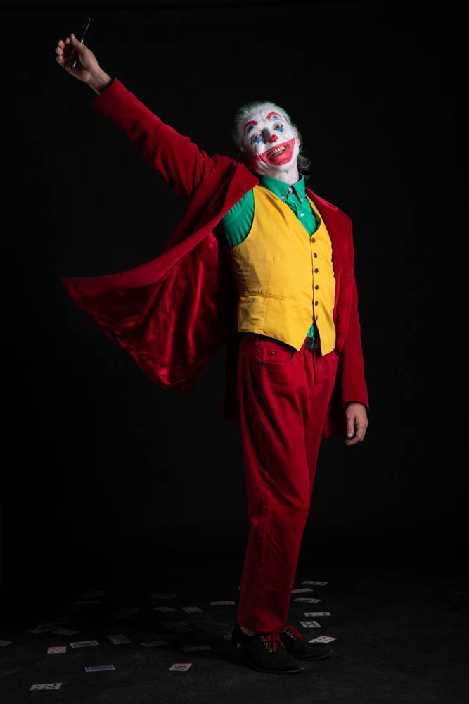 Joker con il braccio teso in alto, la giacca aperta che svolazza e carte da gioco sparse a terra