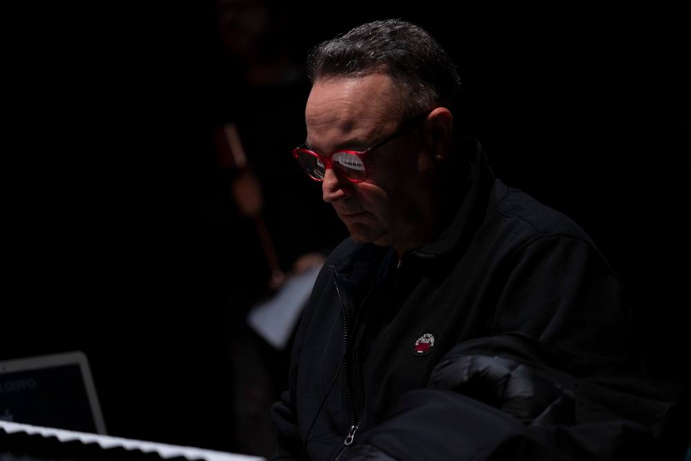 Primo piano in penombra di un uomo con occhiali rossi, che guarda in basso verso una tastiera