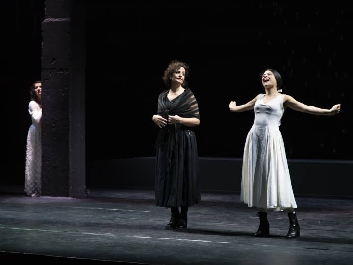 Tre donne in scena, una si affaccia da dietro una colonna